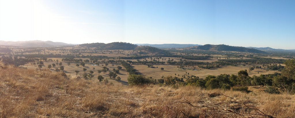 A panorama photo taken from the Baranduda range looking across the Leneva valley, towards the hills around Wodonga - late afternoon sun radiating from the left-hand corner illuminates a dry landscape with brown grass during drought in 2006