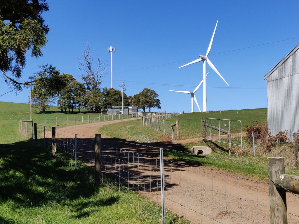 Two wind turbines are seen just over the crest of a grassed hill at Hepburn wind.